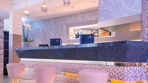 Una zona de bar moderna con encimera de mármol, dos taburetes morados y una pared decorativa con un patrón geométrico.