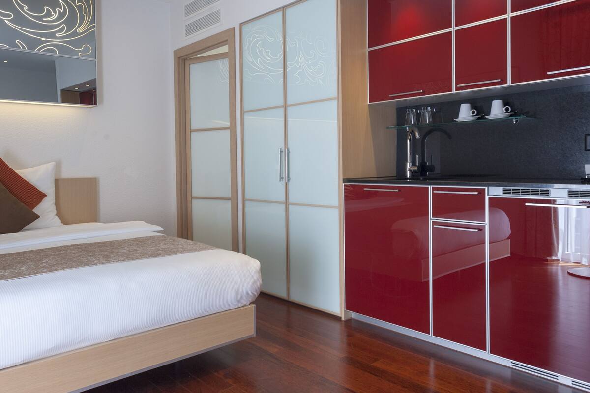 Ein modernes Hotelzimmer mit Bett, Kleiderschrank und einer Küchenzeile.