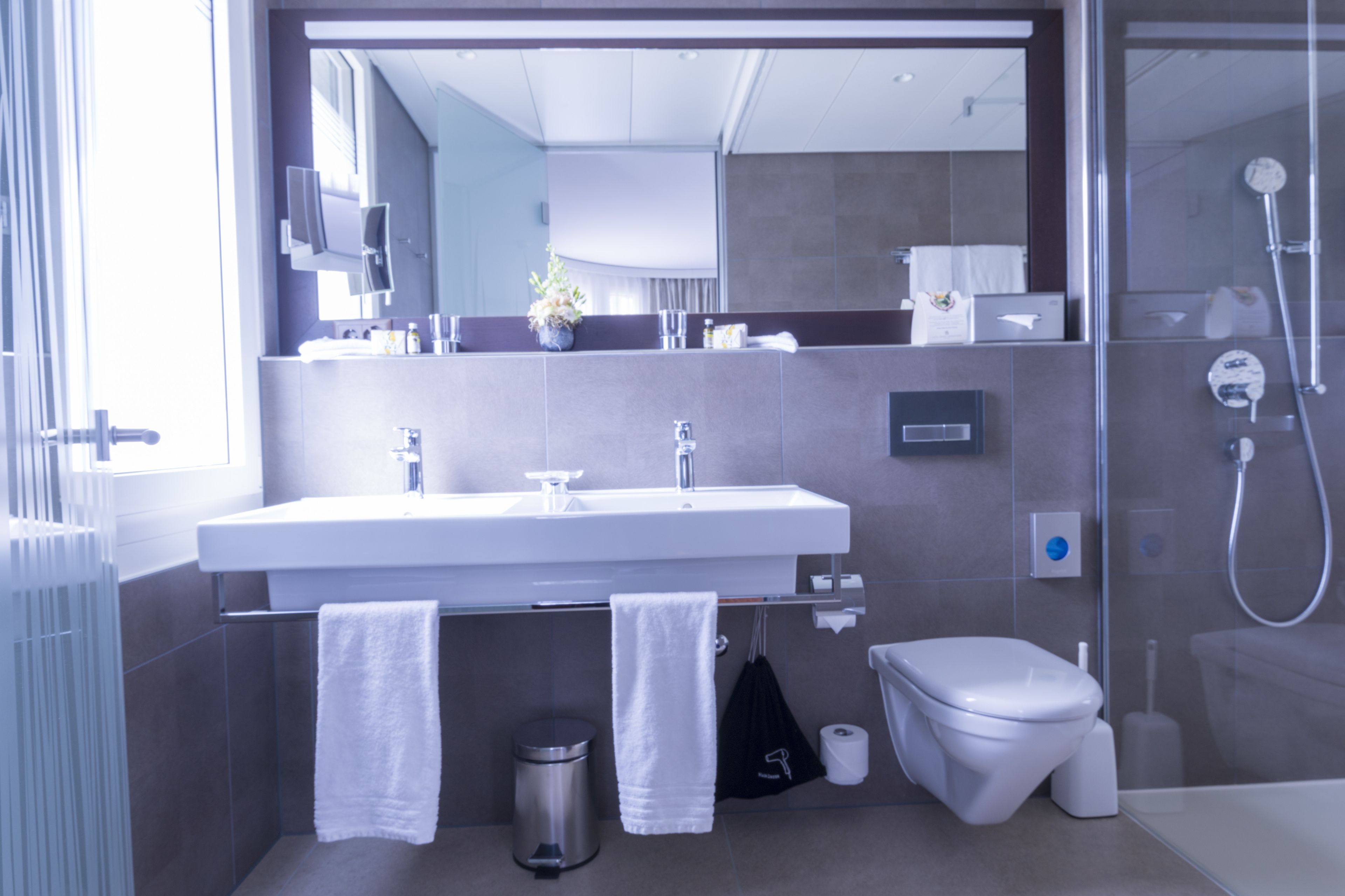 Ein modernes Badezimmer mit großem Spiegel, weißem Waschbecken und einer Duschkabine aus Glas.