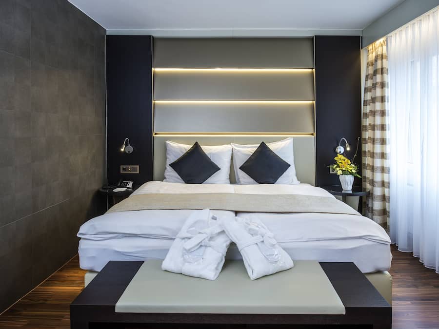 A modern hotel room with a large bed, bedside tables, and a bench with towels.