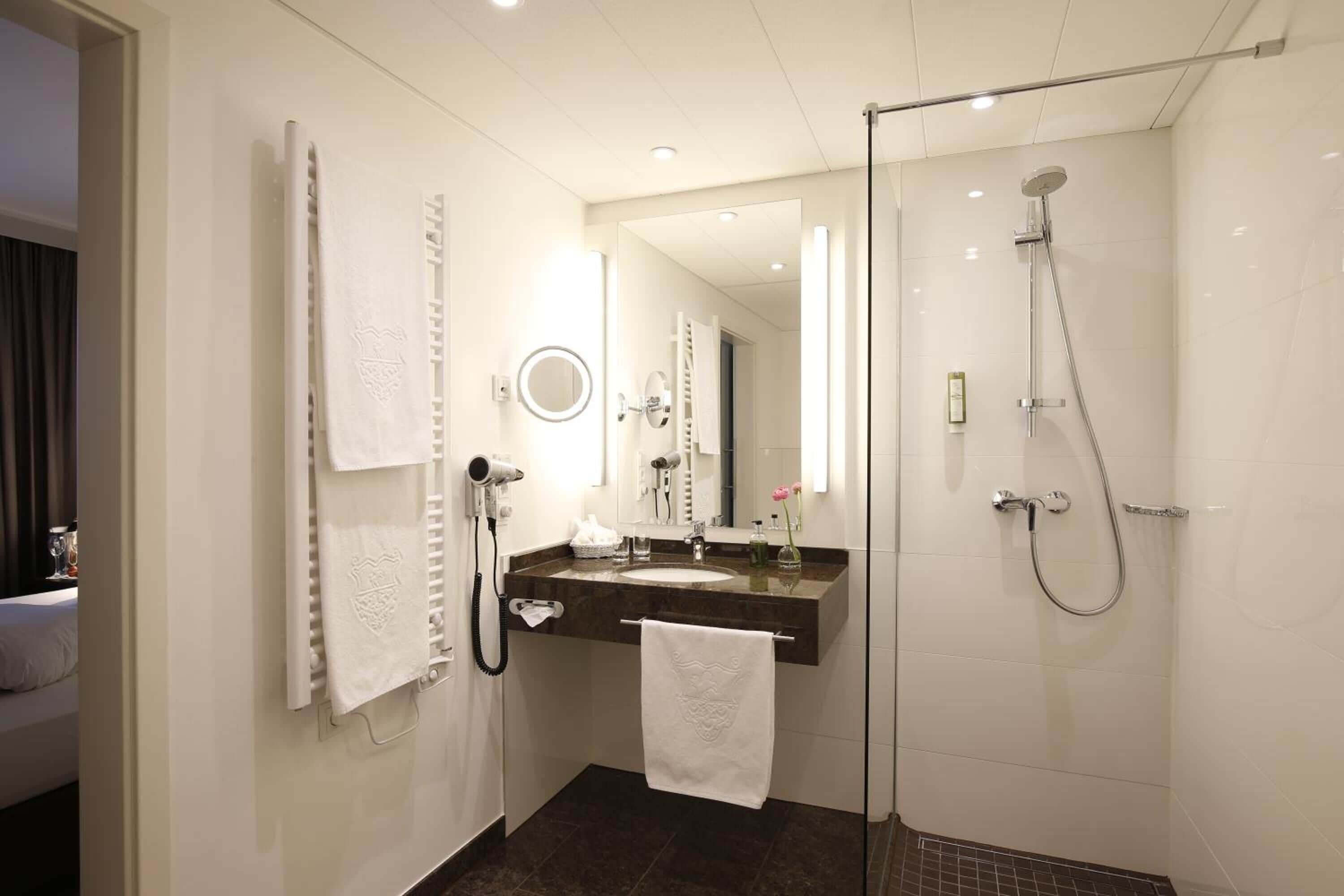 Un baño moderno con cabina de ducha de vidrio, tocador con espejo y toallas colgadas en la pared.