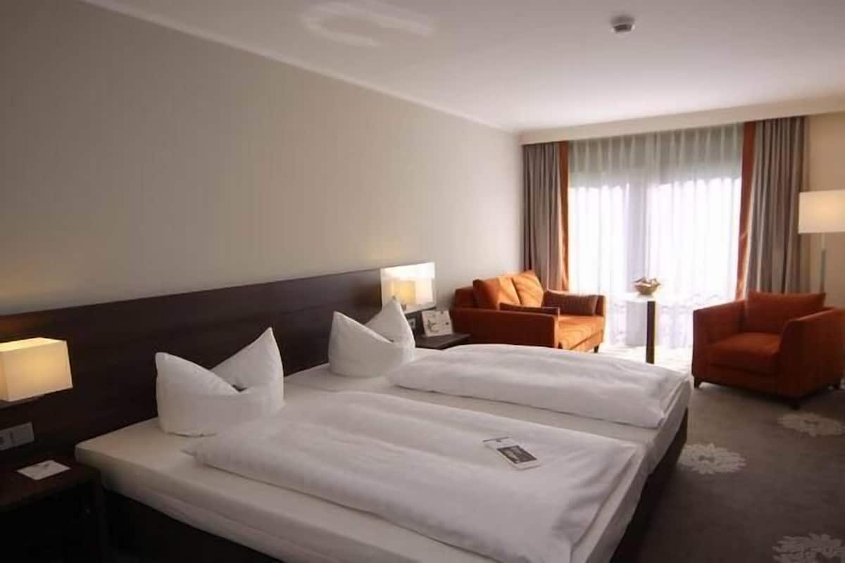 Une chambre d’hôtel avec deux lits, un bureau, une chaise et une fenêtre avec des rideaux.