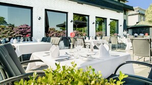 An outdoor dining area with tables set for two, large windows, and a brick building facade. - Parkhotel Wittekindshof Dortmund (Dortmund)