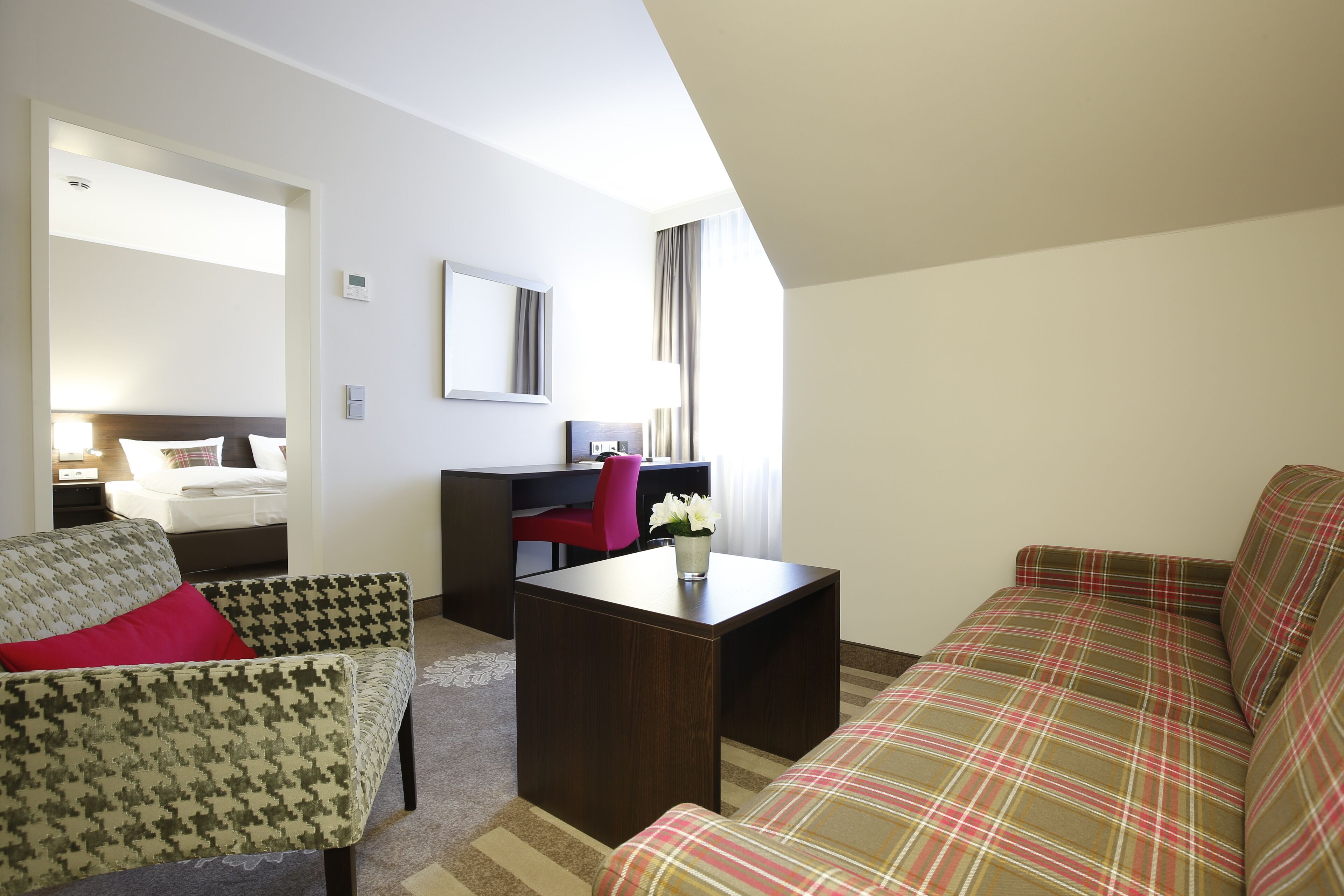 A hotel room with a bed, a desk, a chair, and a sofa.