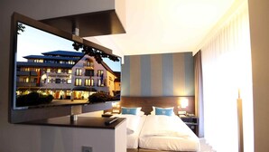 A hotel room with a large bed, a bedside table, a TV mounted on the wall, and a view of the hotel building. - Parkhotel Wittekindshof Dortmund (Dortmund)