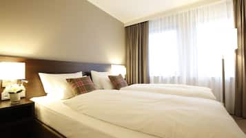 Una habitación de hotel con dos camas, una mesita de noche con lámpara y una ventana con cortinas.