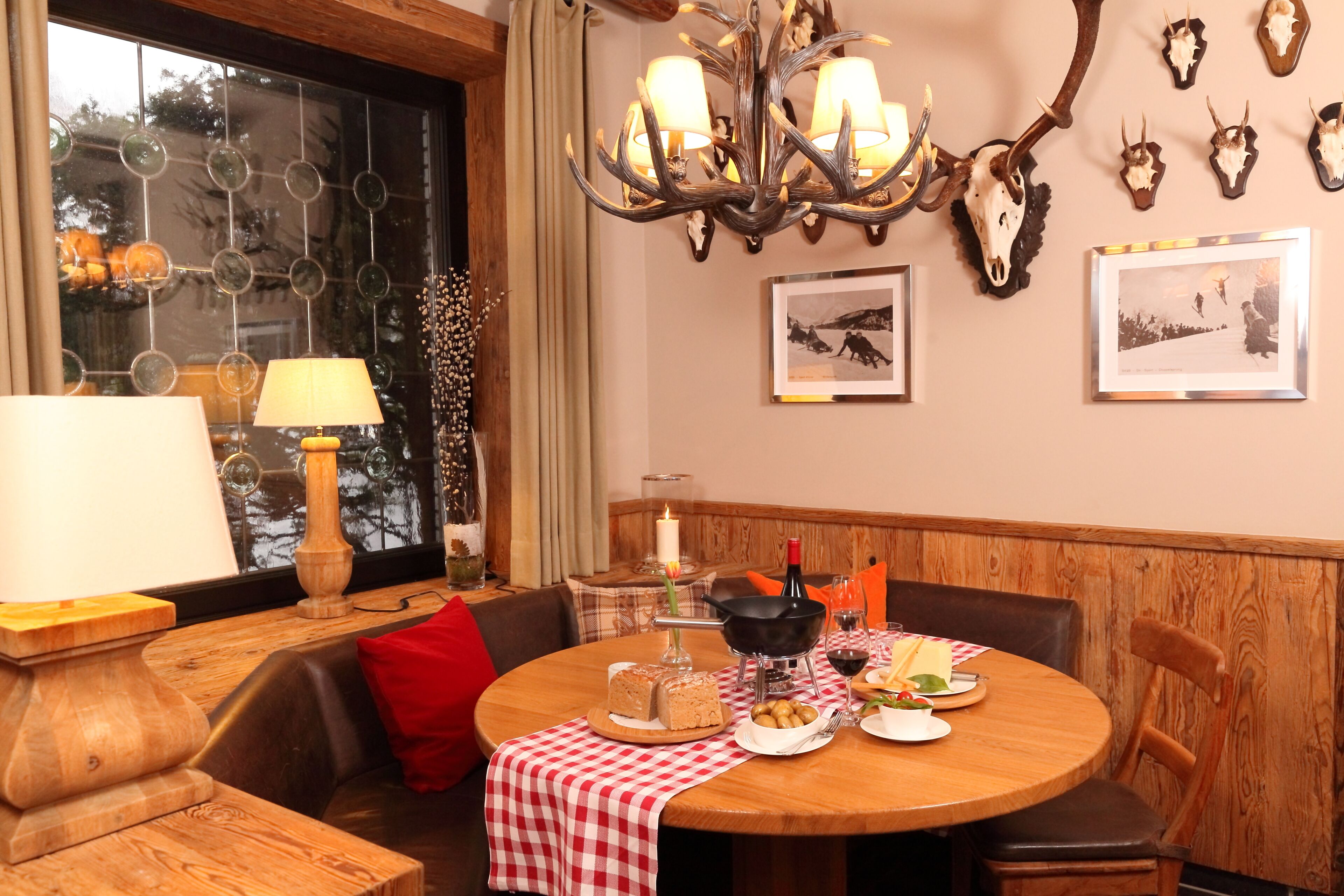 A dining area with a round table, wooden chairs, a chandelier, and wall-mounted animal skulls.