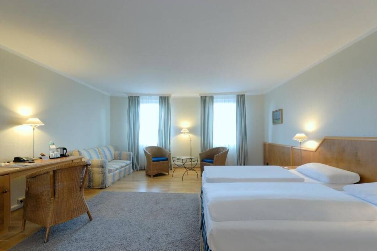 A hotel room with a bed, two chairs, a desk, and a lamp.
