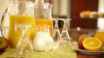 Impostazione colazione con una brocca di succo d'arancia, una caraffa di latte e un piatto di frutta, tra cui una mela e un'arancia.