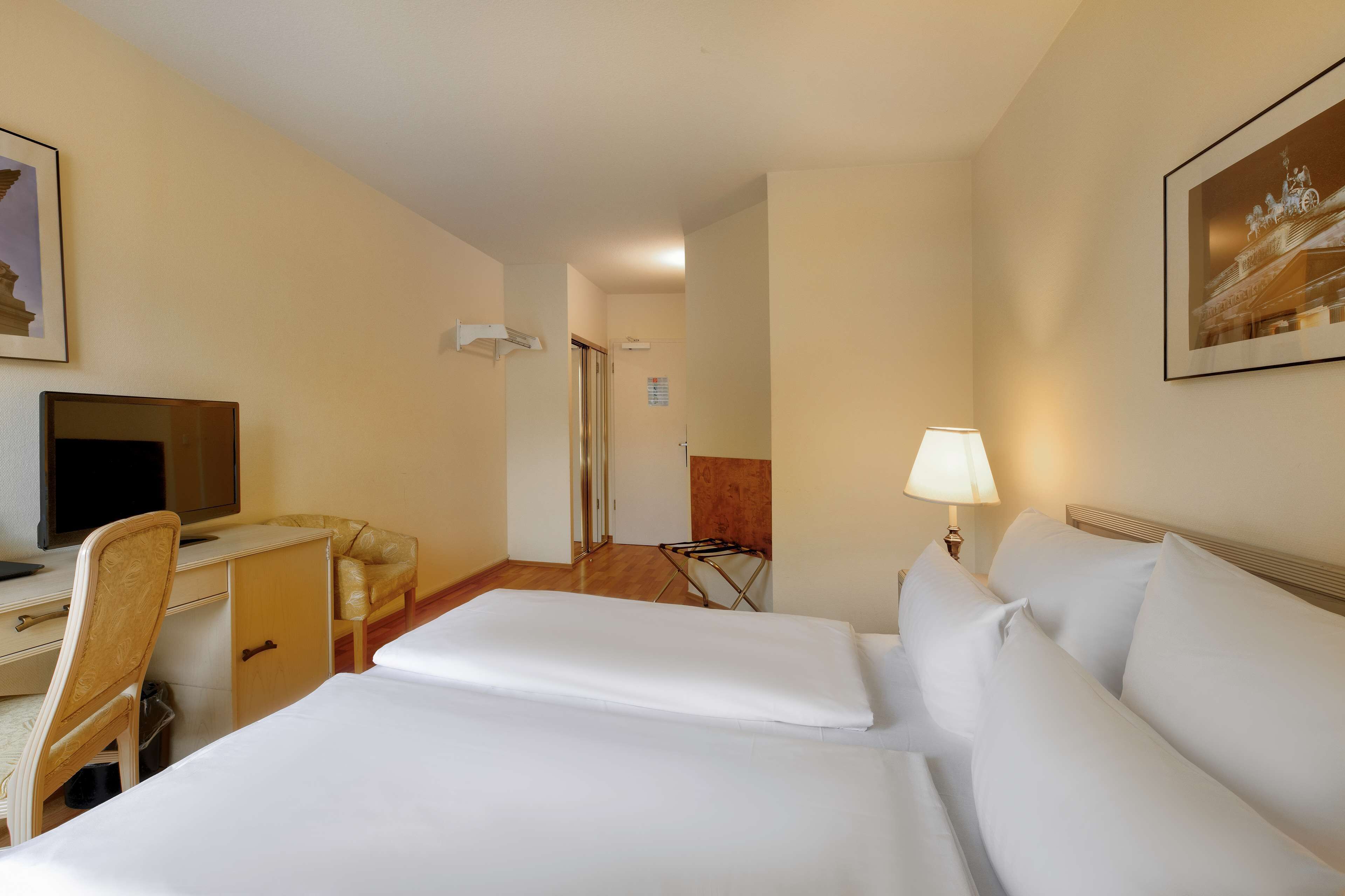 A hotel room with two beds, a desk with a chair, a TV, and a lamp.