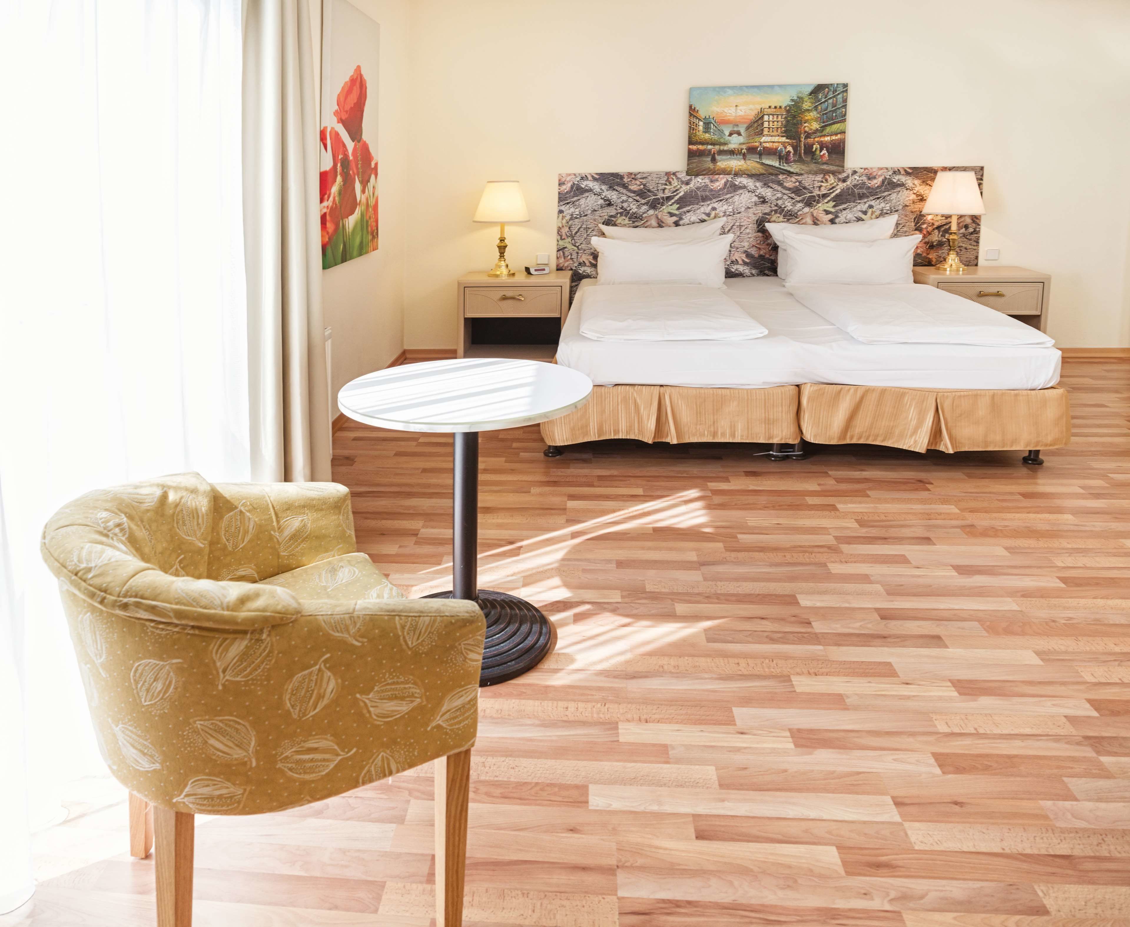 Habitación de hotel con cama, una mesa redonda, una silla y obras de arte en las paredes.