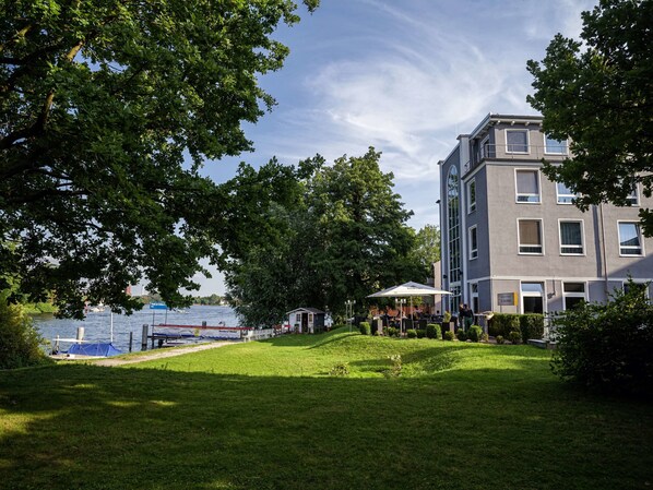 A grassy area with a building, trees, and a body of water in the background.