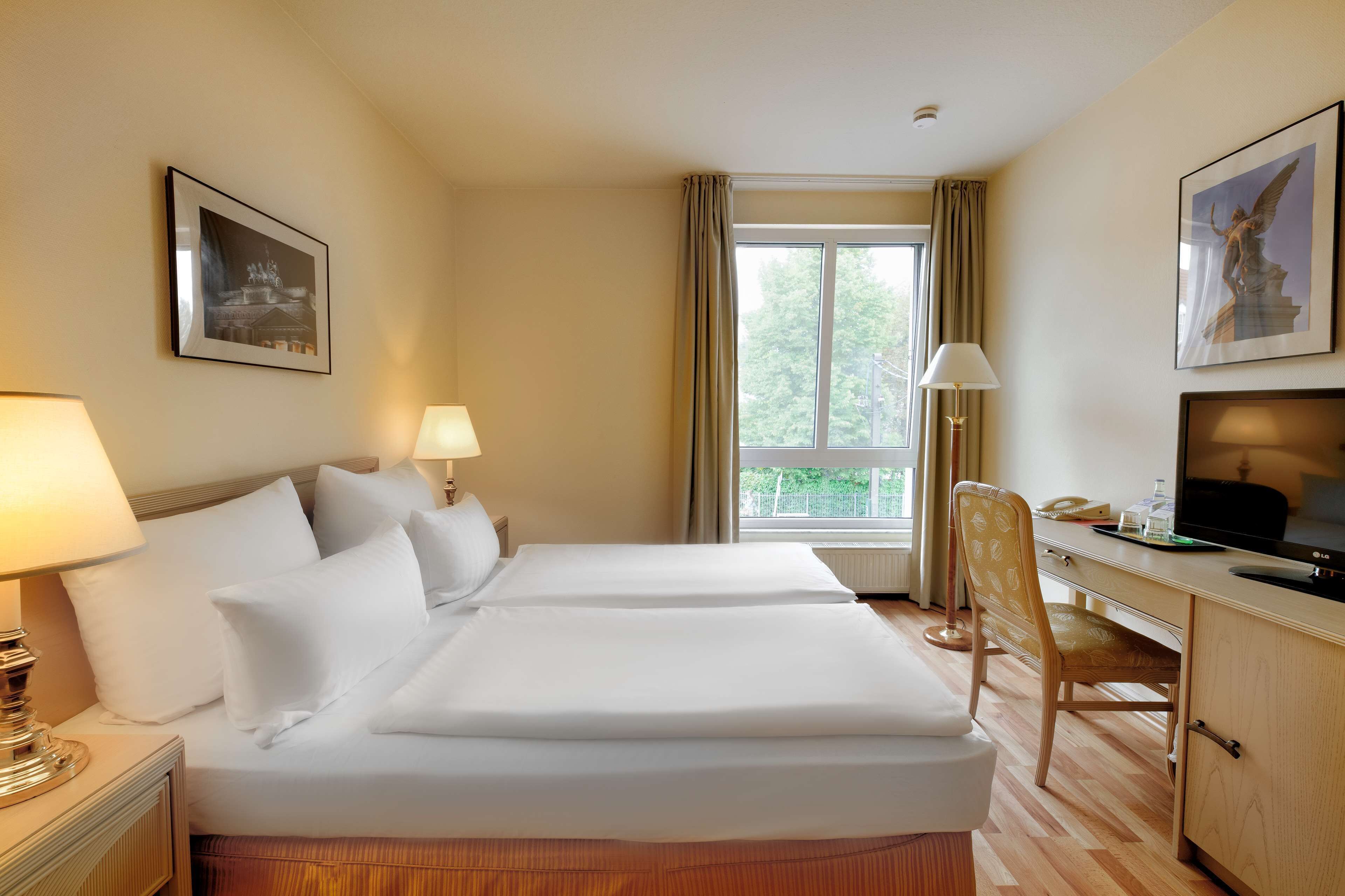 Habitación de hotel con dos camas, un escritorio, una silla, un televisor y una ventana con cortinas.