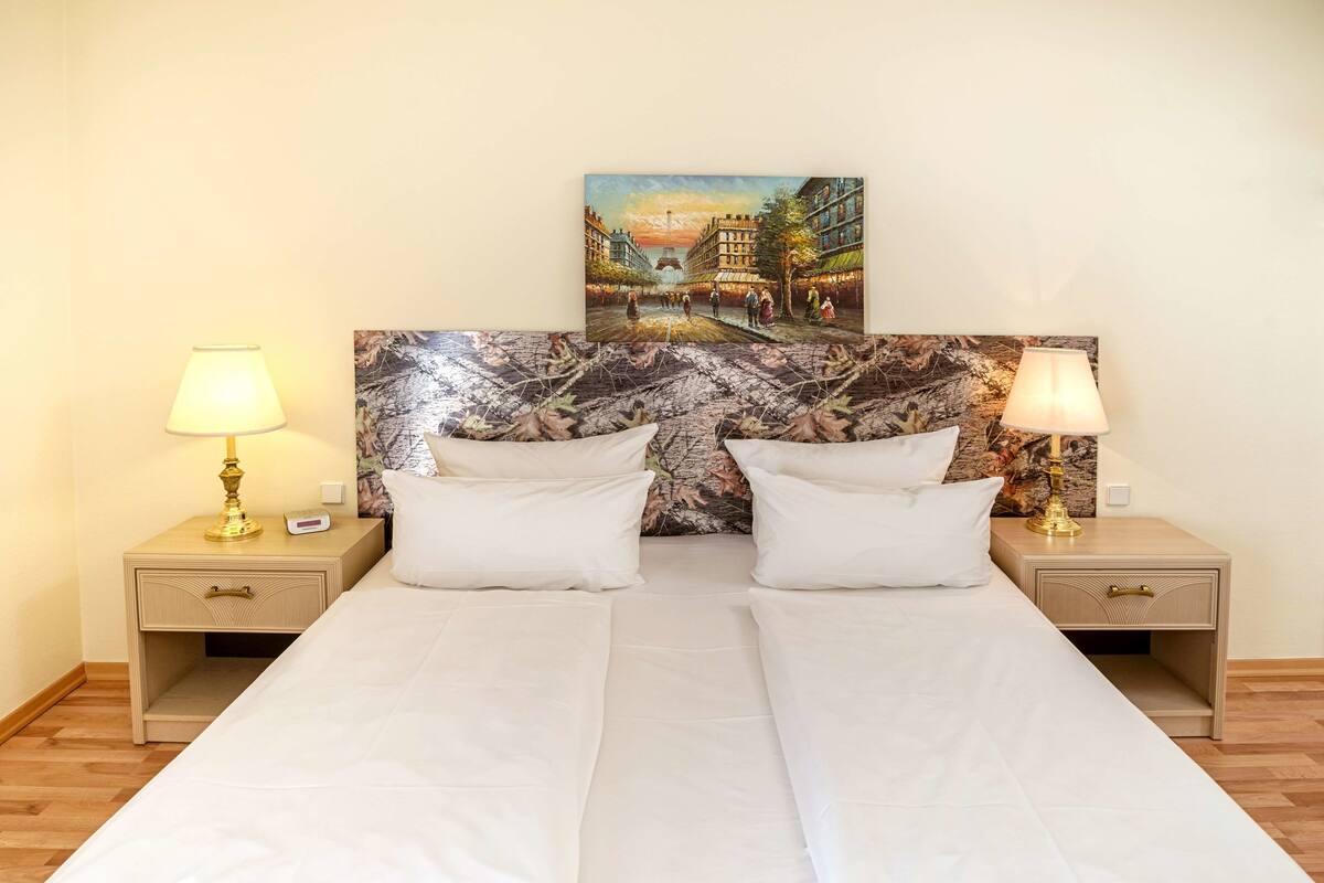 Ein Hotelzimmer mit Doppelbett, zwei Nachttischen mit Lampen, einem Gemälde an der Kopfteil und Holzboden.