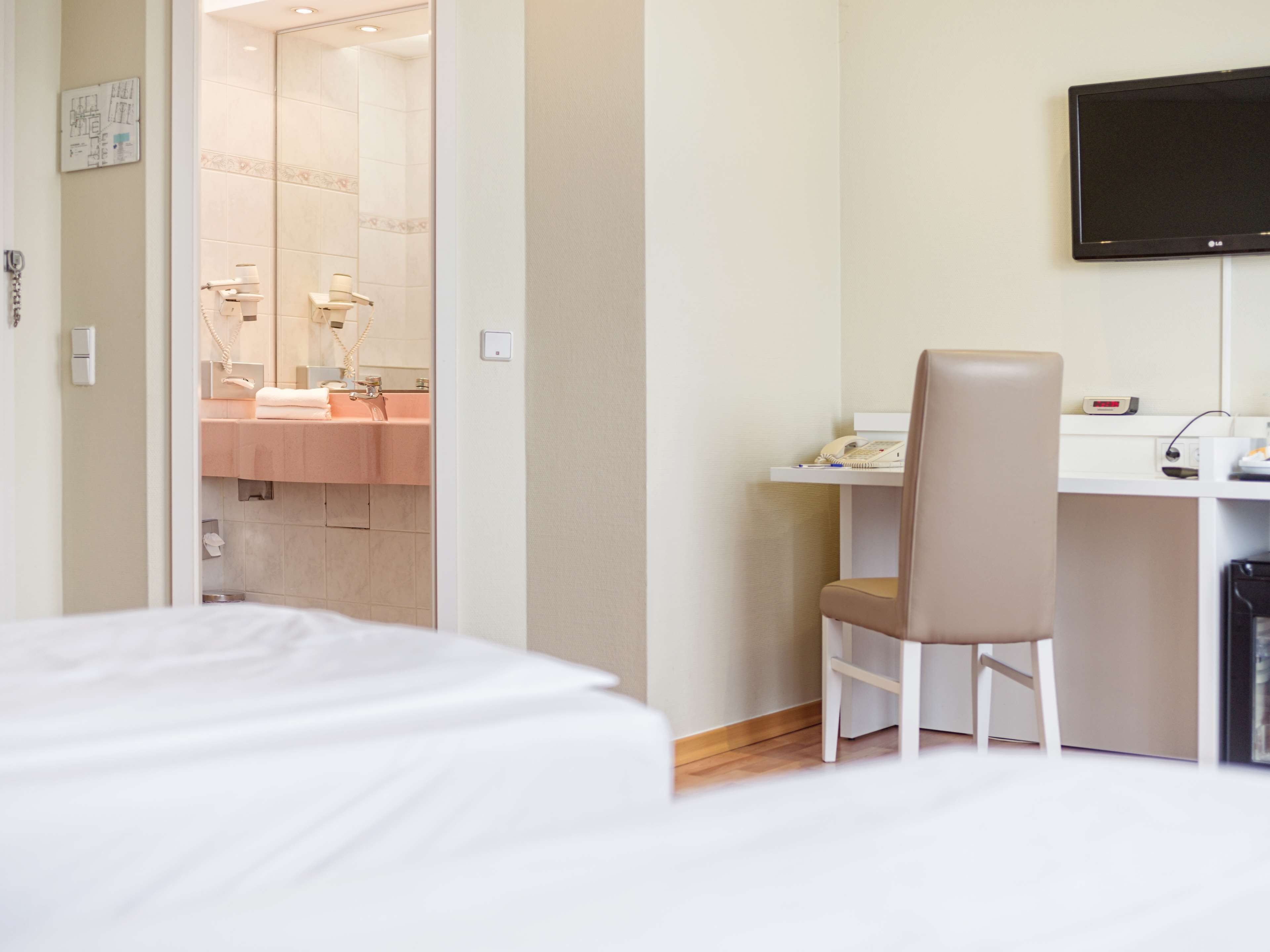 Habitación de hotel con cama, escritorio con silla, televisión y baño visible a través de una puerta abierta.