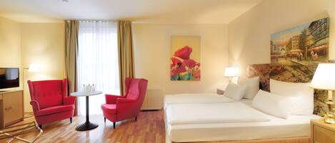 A hotel room with a wooden floor, a bed, two red chairs, a small table, a TV, and a painting on the wall.