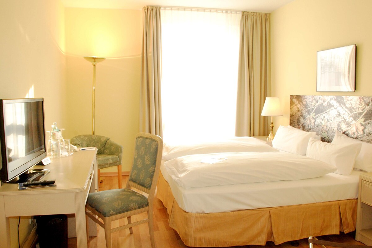 Une chambre d’hôtel avec un lit, un bureau avec une télévision, une chaise, une lampe et un tableau au mur.