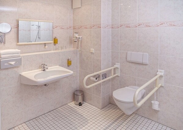 A modern bathroom with a sink, mirror, toilet, and grab bars. - Hotel Am Schloss Koepenick Berlin by Golden Tulip (Berlin)