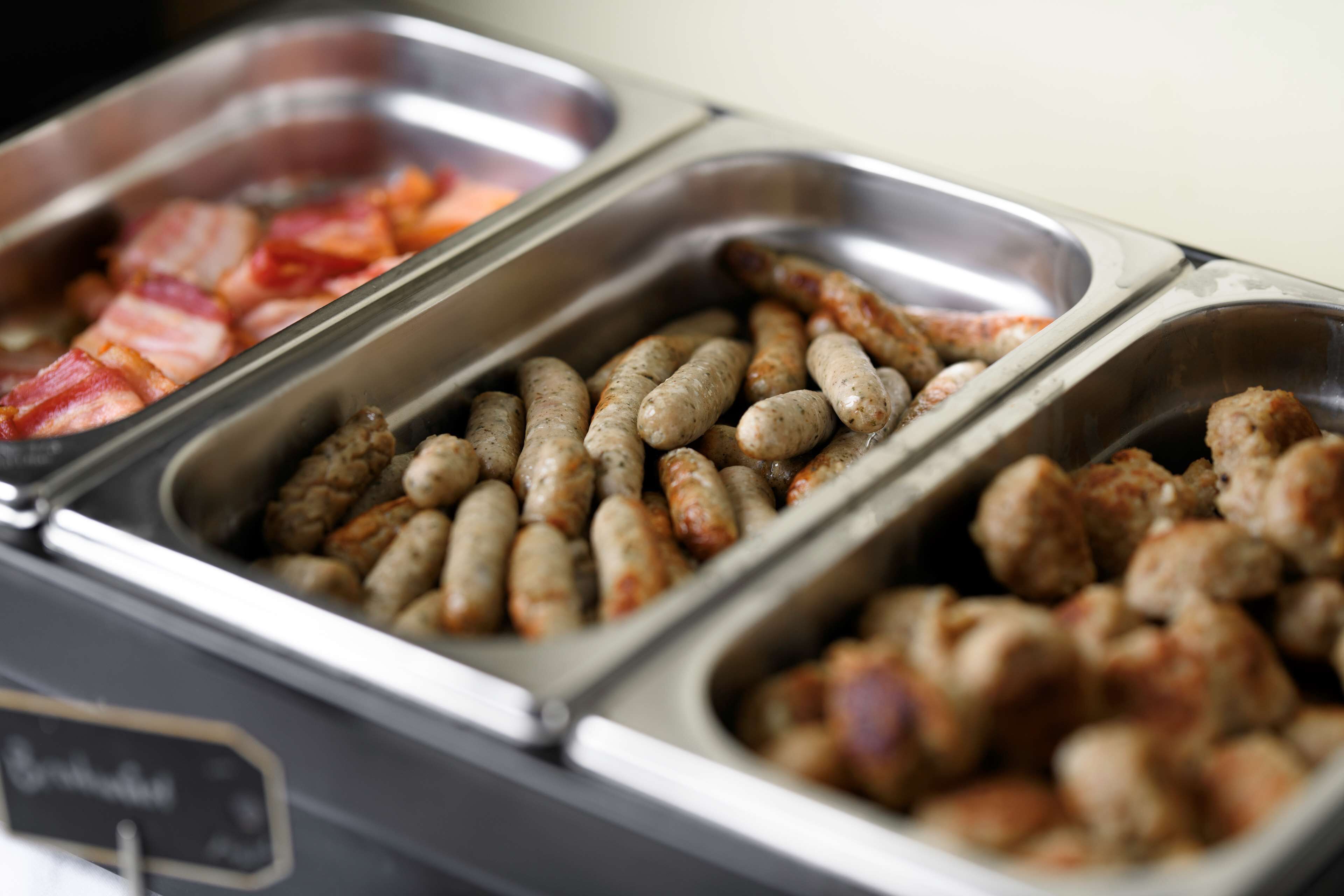 Een ontbijtbuffet met diverse gerechten, waaronder bacon, worst en ander vlees.