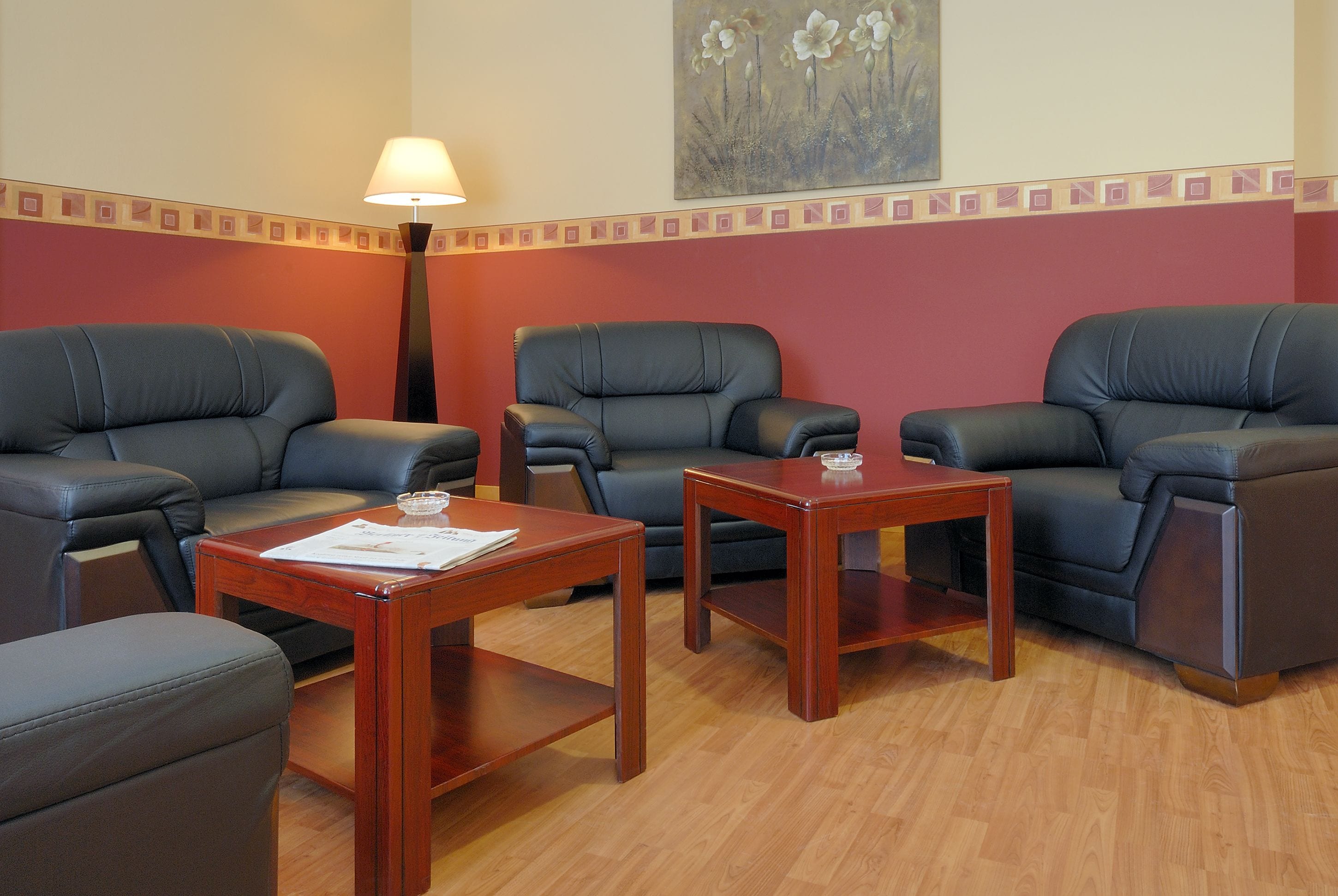 A room with three leather sofas, two wooden side tables, and a floor lamp.