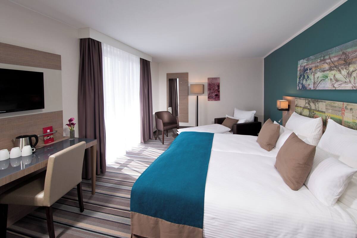 A hotel room with a large bed, a desk with a flat-screen TV, a chair, and a painting on the wall.