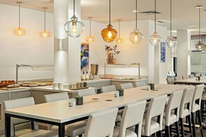 A modern dining area with long tables, chairs, and pendant lighting. - Leonardo Hotel Munich City Olympiapark (Munich)
