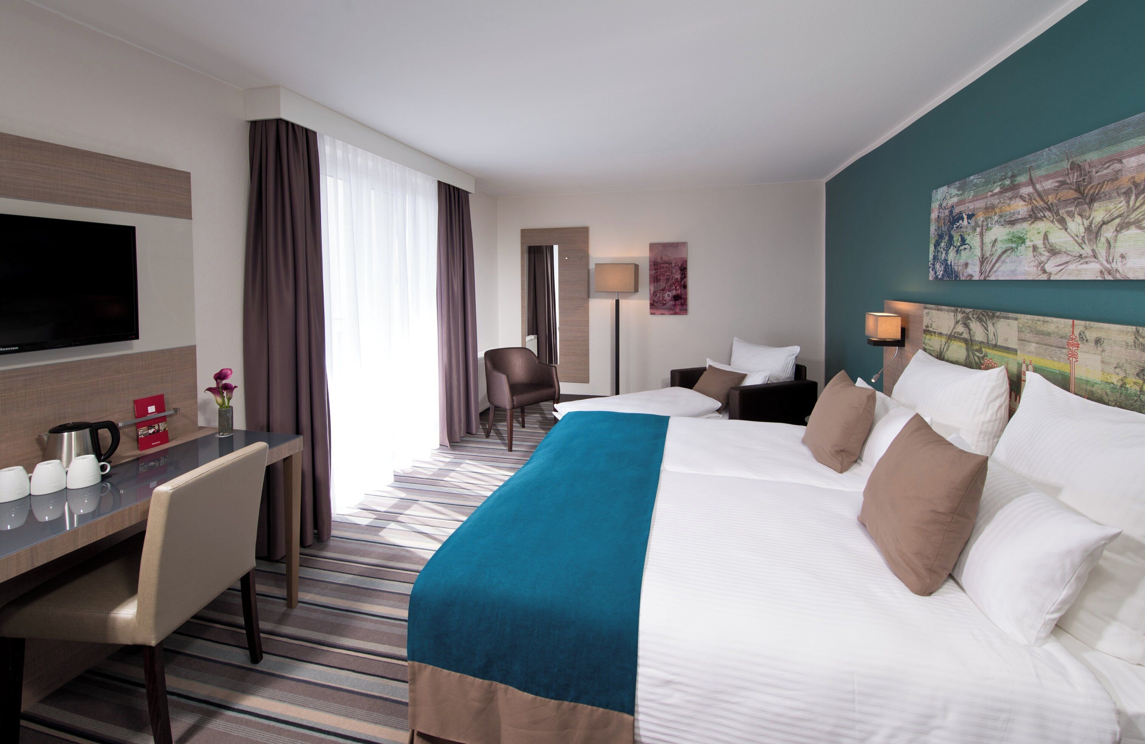 A hotel room with a large bed, a desk with a flat-screen TV, a chair, and a painting on the wall.