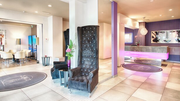 A modern hotel lobby with a reception desk, seating area, and a decorative column. - Leonardo Hotel Munich City Olympiapark (Munich)