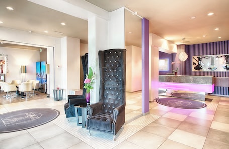 A modern hotel lobby with a reception desk, seating area, and a decorative column.
