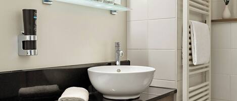 A bathroom with a white vessel sink, a black countertop, a towel, a glass soap dispenser, and a towel rack.