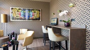 Un área de bar moderna con pared de patrón geométrico de espiga, un cuadro abstracto grande, un monitor de computadora y un florero con flores.