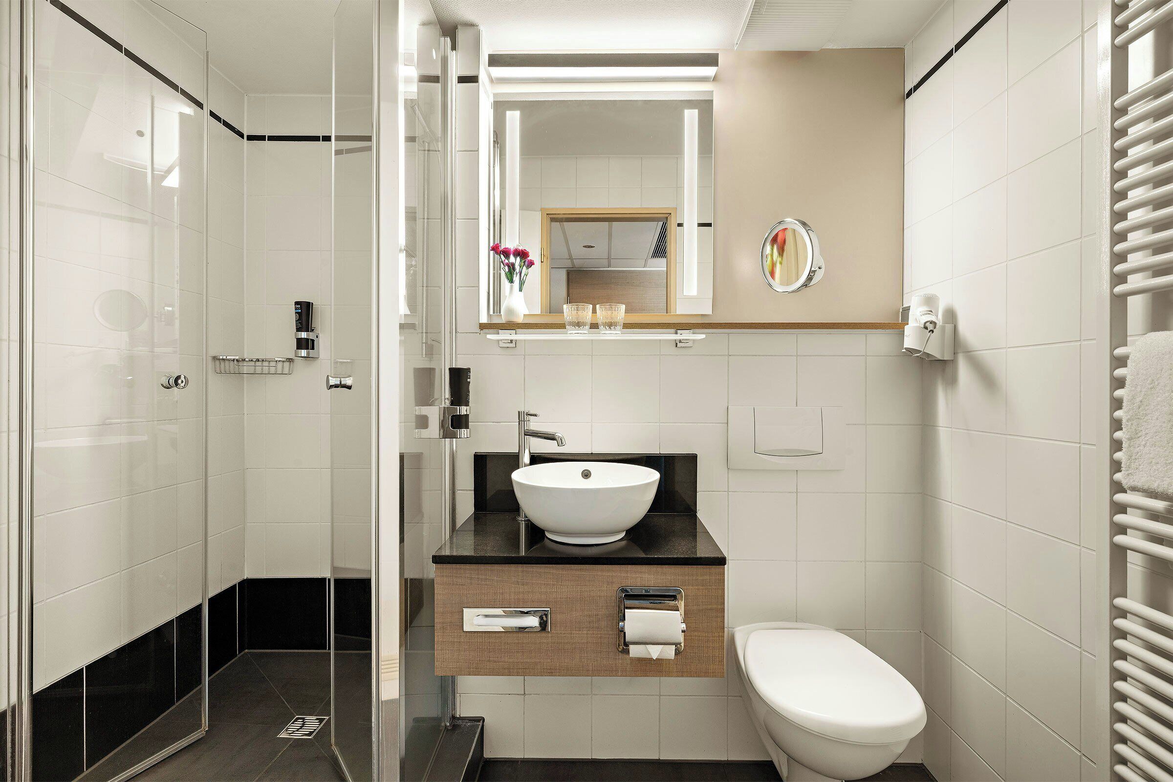Un baño moderno con cabina de ducha de vidrio, un lavamanos blanco sobre encimera negra y un inodoro blanco.