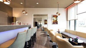 A modern bar area with bar stools, a seating area with sofas, and pendant lighting. - Leonardo Hotel Munich City Olympiapark (Munich)