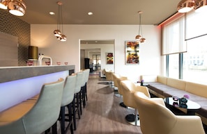 A modern bar area with bar stools, a seating area with sofas, and pendant lighting. - Leonardo Hotel Munich City Olympiapark (Munich)