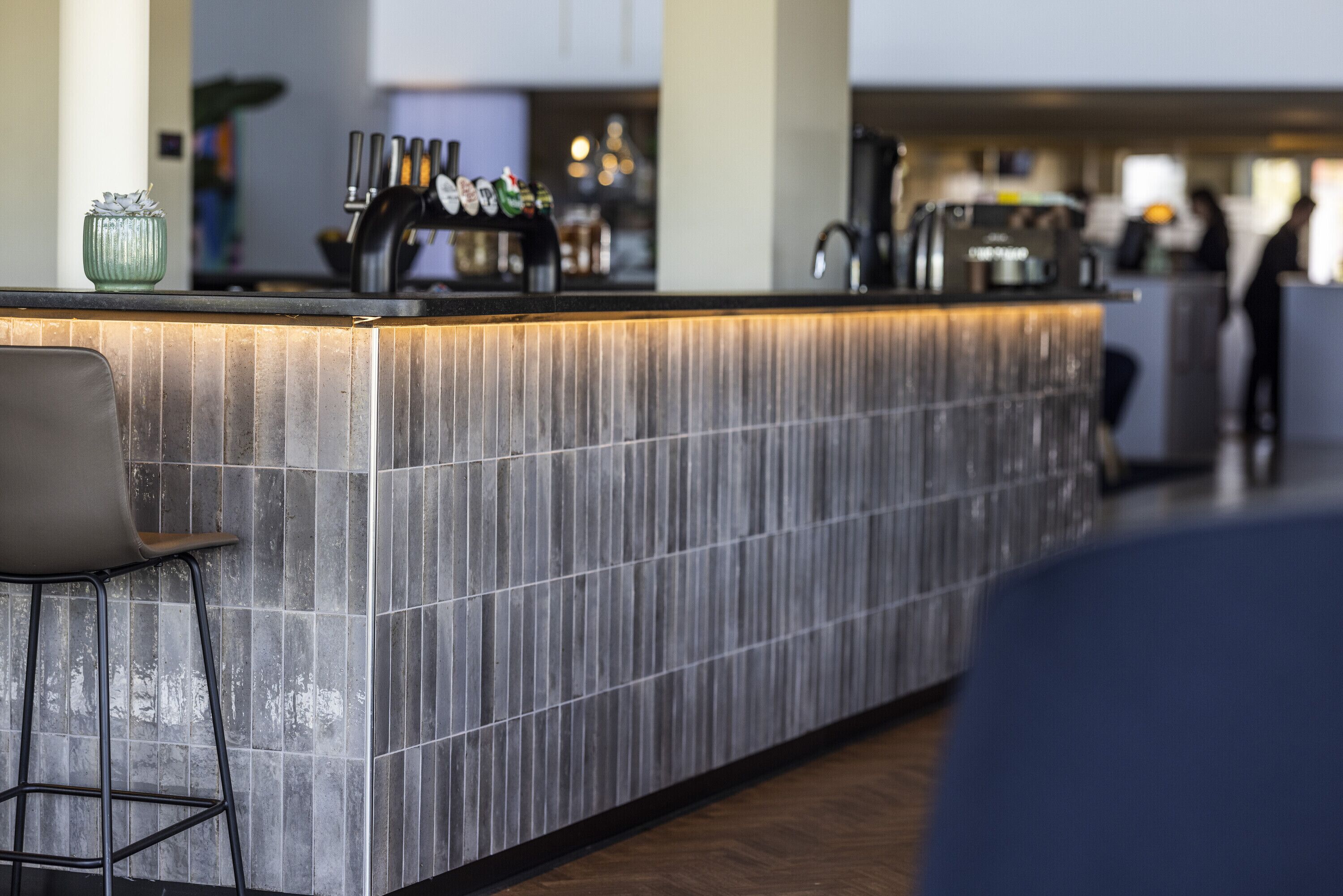 A modern kitchen with a long island counter, bar stools, and a coffee machine.