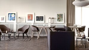 Une chambre d’hôtel moderne dotée d’un coin salon, d’œuvres d’art au mur et d’une grande fenêtre avec des rideaux.