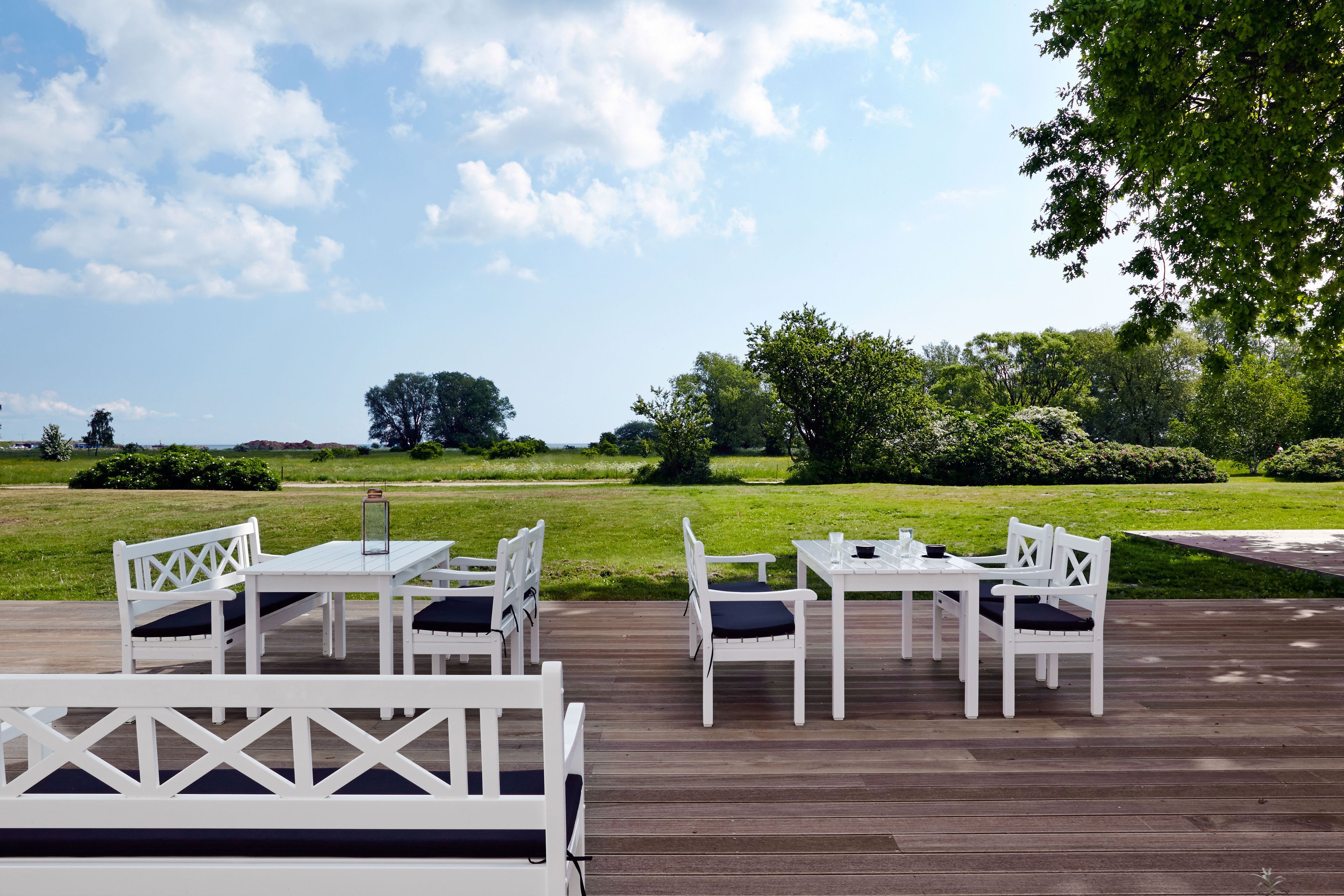 Terraza exterior con mobiliario blanco y vista a un paisaje con césped.