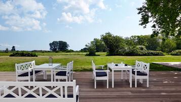 Terraza exterior con mobiliario blanco y vista a un paisaje con césped.