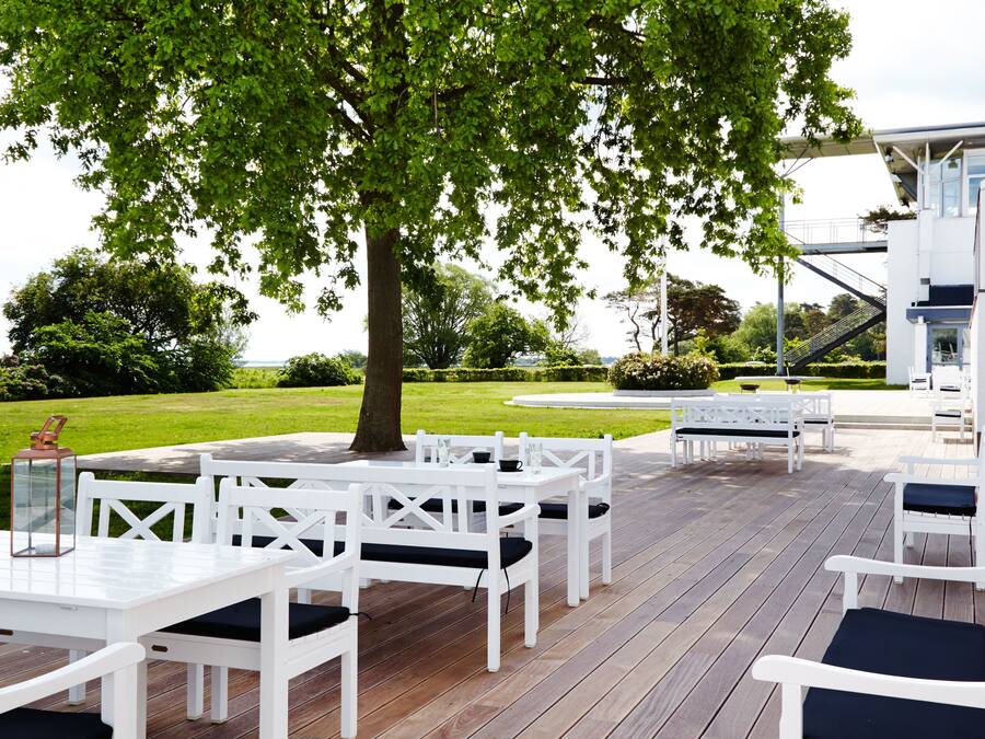 An outdoor patio with white wooden furniture and a large tree providing shade.