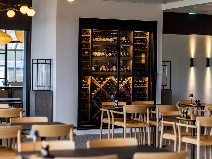 Un interior moderno con una cava de vinos, sillas y mesas de madera.