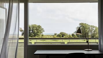 Una habitación con escritorio y lámpara cerca de una ventana que da a un área verde y árboles.