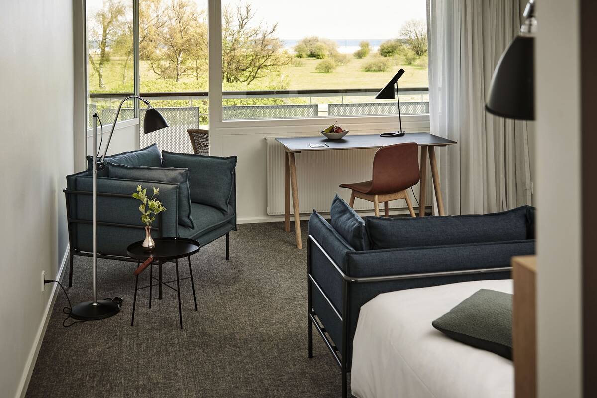 Ein Hotelzimmer mit Bett, Schreibtisch, Stuhl, Sofa und Blick ins Freie.