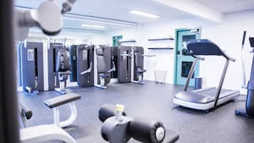 Ein Fitnessstudio mit verschiedenen Trainingsgeräten, Laufband und einer Bankpresse.