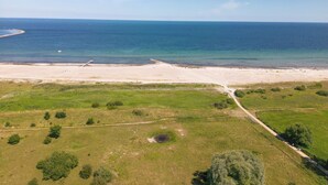 Une vue aérienne d’une plage, avec un ciel dégagé, un rivage sablonneux et une végétation verdoyante.