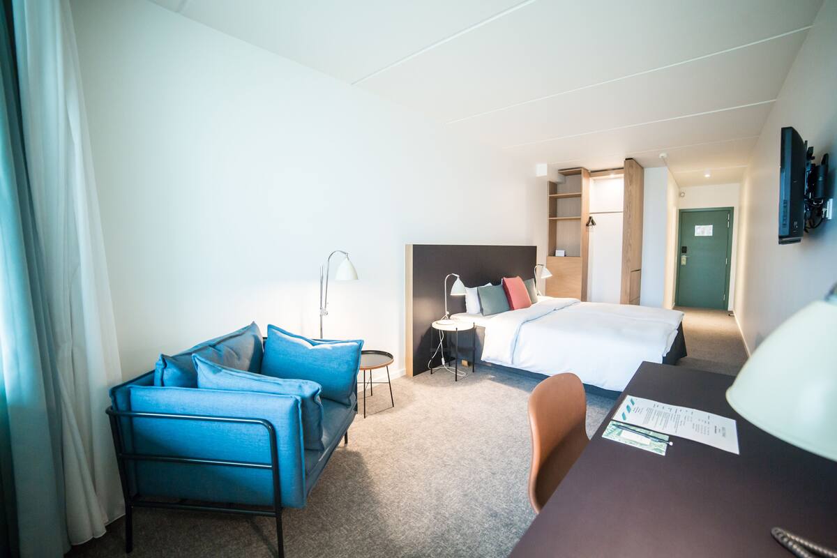 Ein Hotelzimmer mit Bett, Schreibtisch, Sessel, Sofa, Lampe und Fernseher.