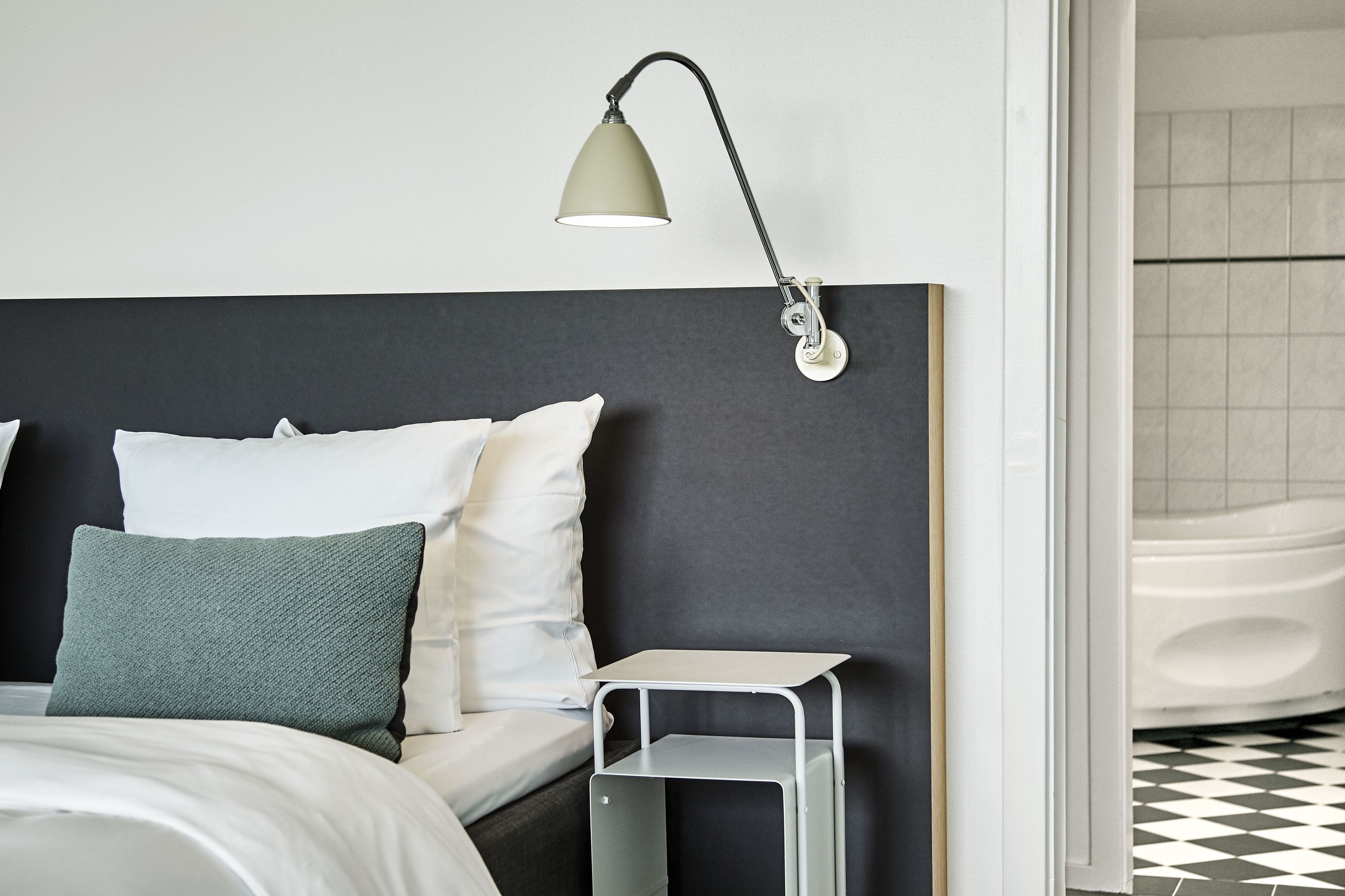 A modern bedroom with a bed, pillows, a nightstand, and a wall-mounted lamp.
