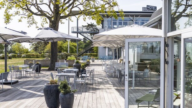 Une terrasse extérieure avec des tables et des chaises, de grands parasols et des plantes en pot.