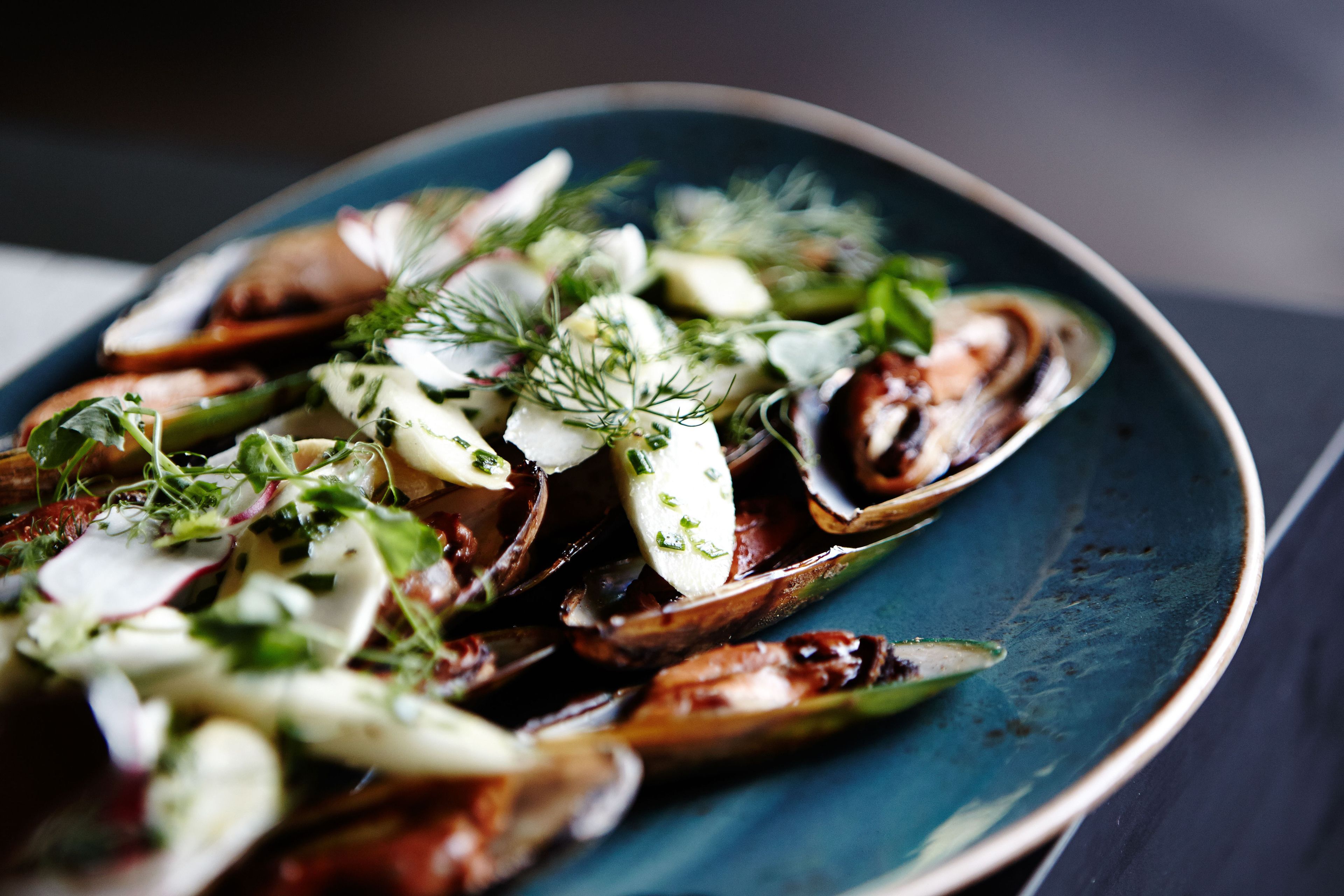 Un plato de mejillones con hierbas y vegetales verdes.