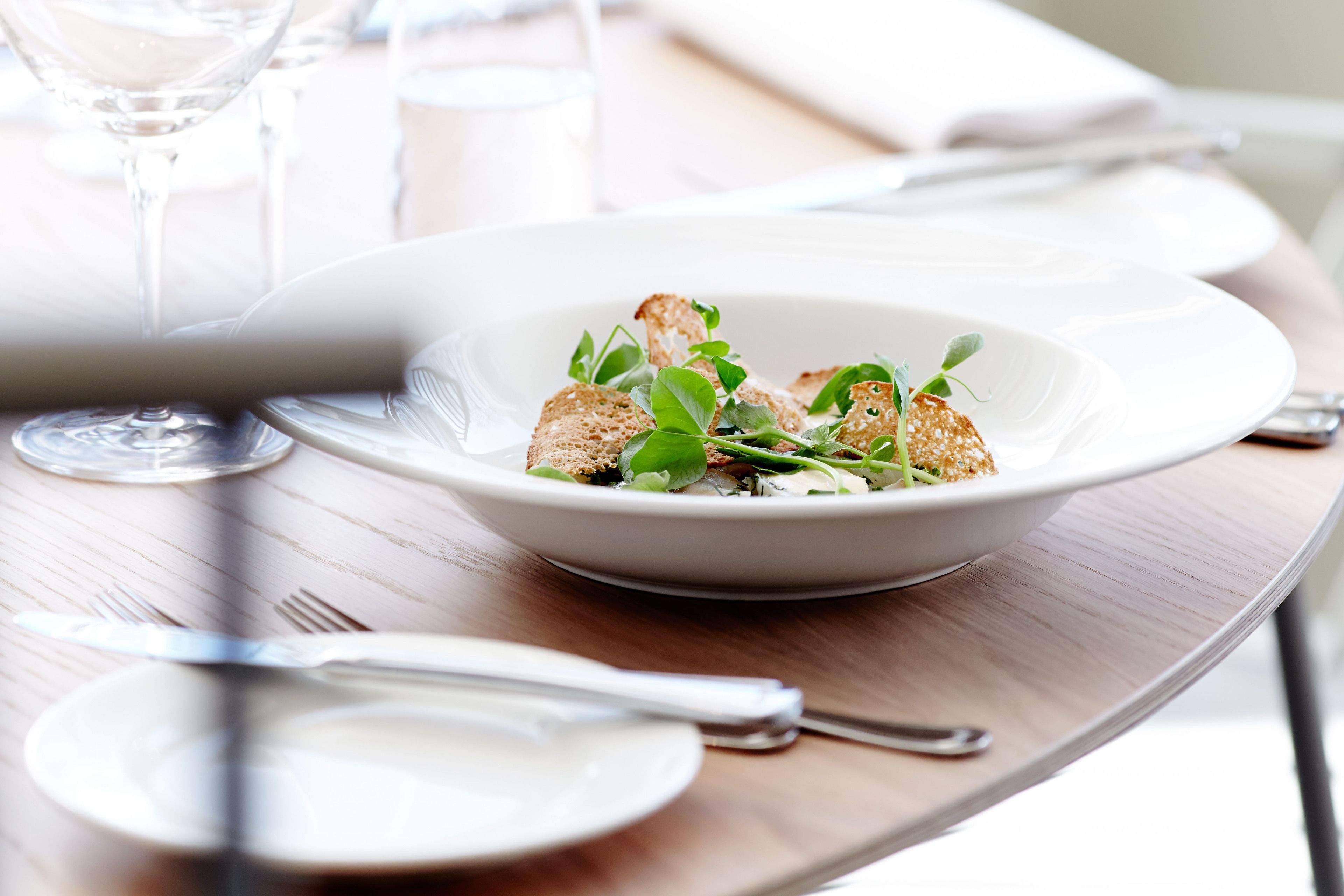 A dining table with a white plate containing a salad, a fork, and a knife.