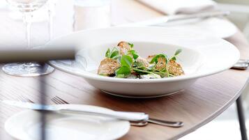 A dining table with a white plate containing a salad, a fork, and a knife.